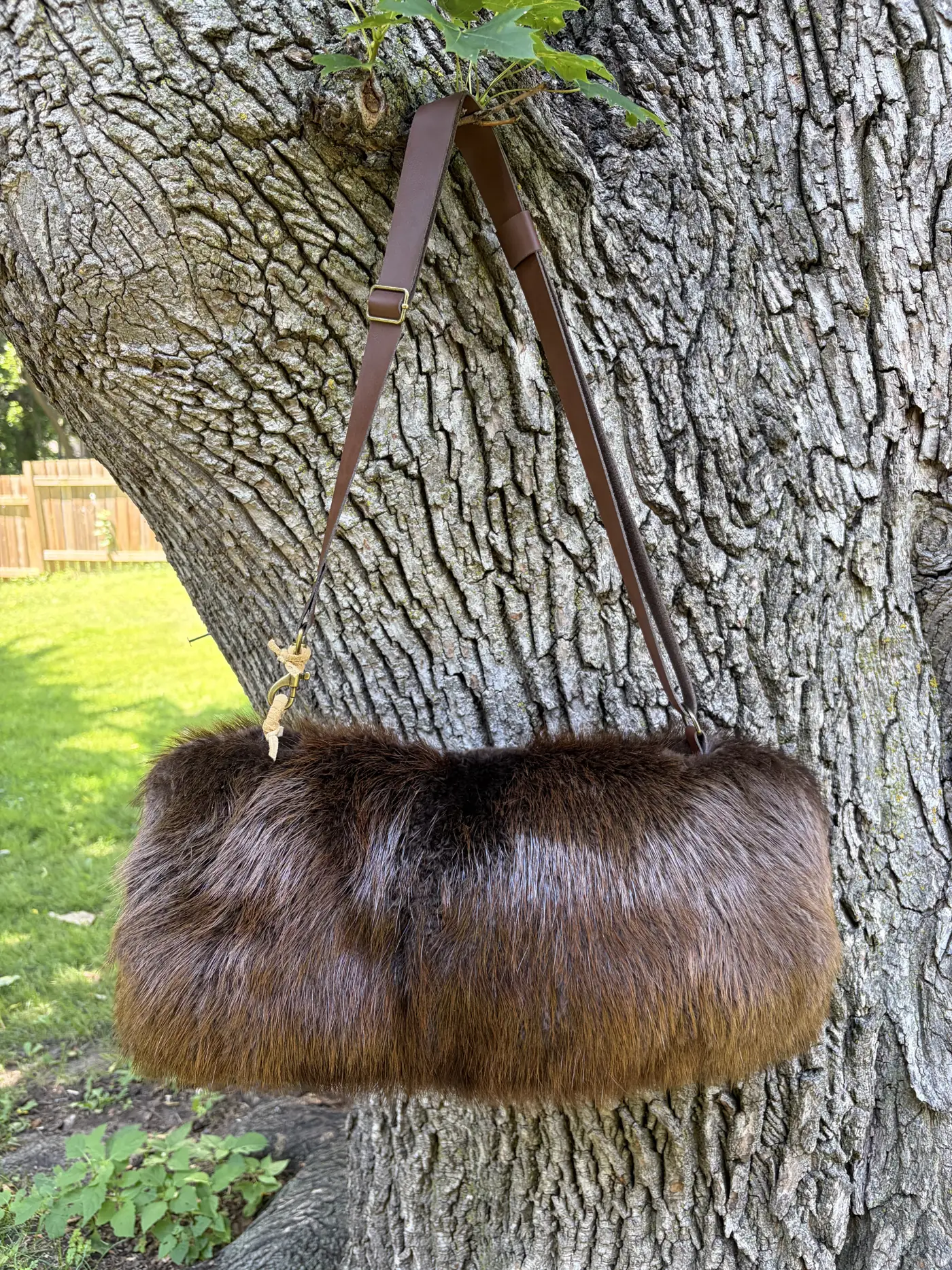Beaver fur hand muff with a leather shoulder strap hanging from a tree